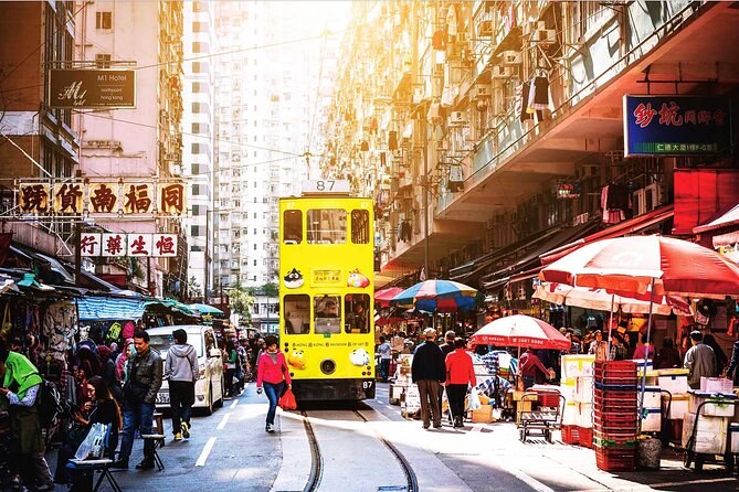 A double-decker tram running through a street of shops and market stalls